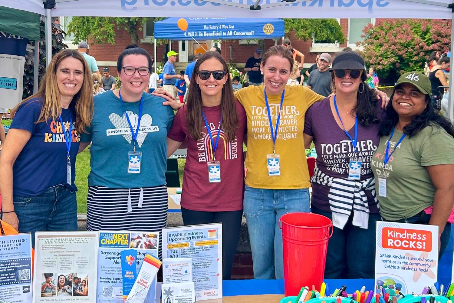 Image of group of SPARK Kindness Team members behind a table under the SPARK Kindness tent at Natick Days 2024, a community event.