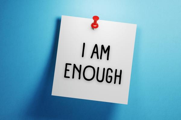 On a blue background is a pinned white square note with handwritten text "I am enough".