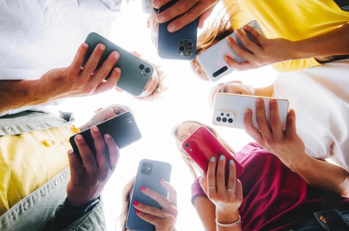 Image perspective from the ground looking up of group of teens each holding and looking at a cell phone